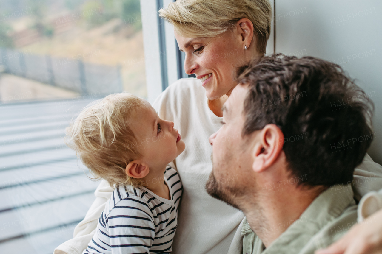 Parents playing with little son, sitting by window. Bonding moment.