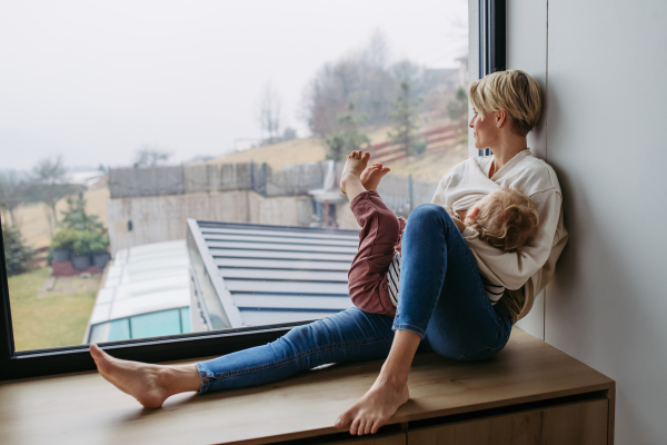 Mother breastfeeding her toddler son, sitting by the window