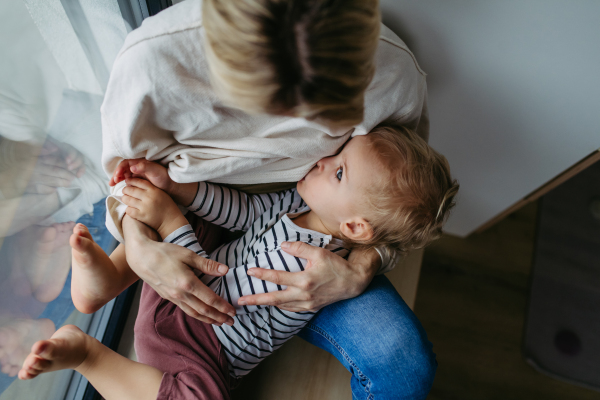 Mother breastfeeding her toddler son, sitting by the window