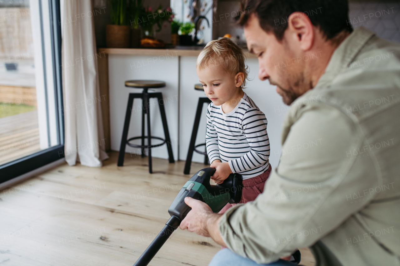 Little boy and dad vacuuming floors with a vacuum cleaner, helping with house chores.