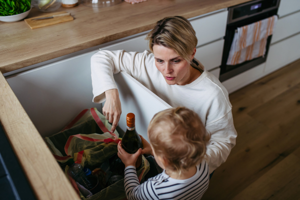 Mother teaching toddler boy to sort waste into recycling bin.