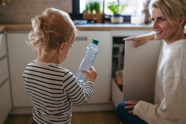 Mother teaching toddler boy to sort waste into recycling bin.