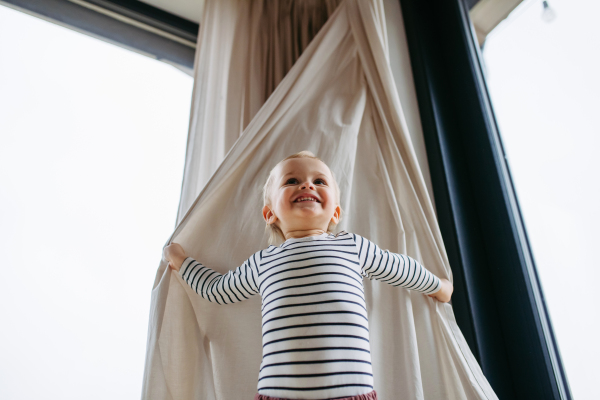 Adorable toddler boy playing hide and seek at home. Low angle view.