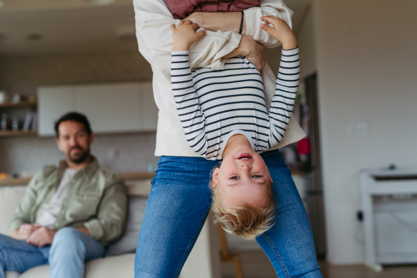 Playful father holding little son upside down, laughing.