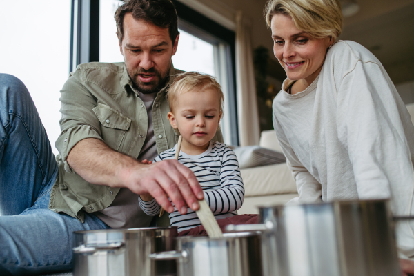 Parents and little toddler son playing drums on kitchen pots.