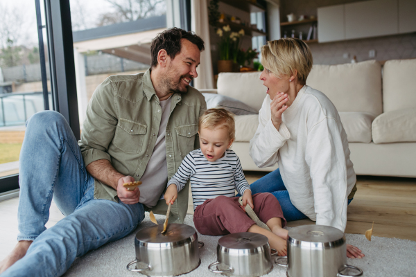 Parents and little toddler son playing drums on kitchen pots.