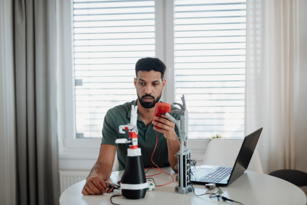 Engineer testing robotic arm circuitry using a multimeter during home robotics project.