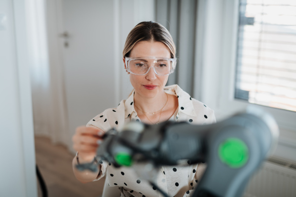 Female engineer building and programming a robotic arm at home. Robotics concept.