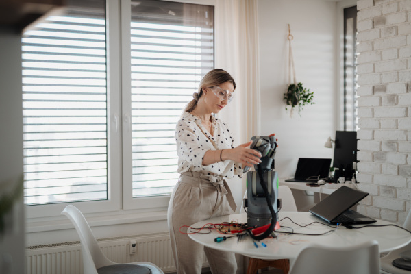 Female engineer building and programming a robotic arm at home. Robotics concept.