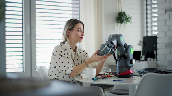 Female engineer building and programming a robotic arm at home. Robotics concept.