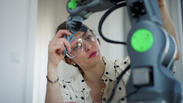 Female engineer building and programming a robotic arm at home. Robotics concept.