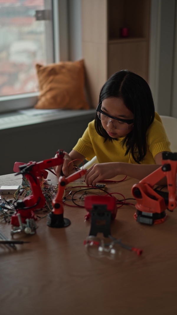 Curious young Japanese girl assembling her first DIY robot at home, exploring robotics and STEM education through hands-on learning. Concept of creativity, innovation, and girls in technology.