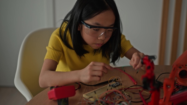 Curious young Japanese girl assembling her first DIY robot at home, exploring robotics and STEM education through hands-on learning. Concept of creativity, innovation, and girls in technology.