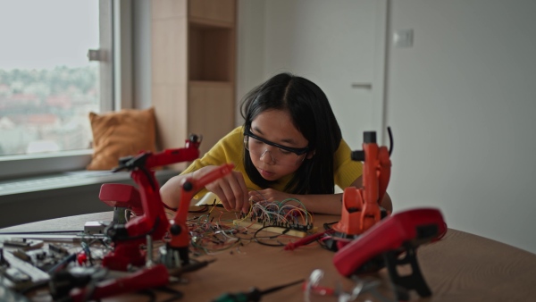 Curious young Japanese girl assembling her first DIY robot at home, exploring robotics and STEM education through hands-on learning. Concept of creativity, innovation, and girls in technology.