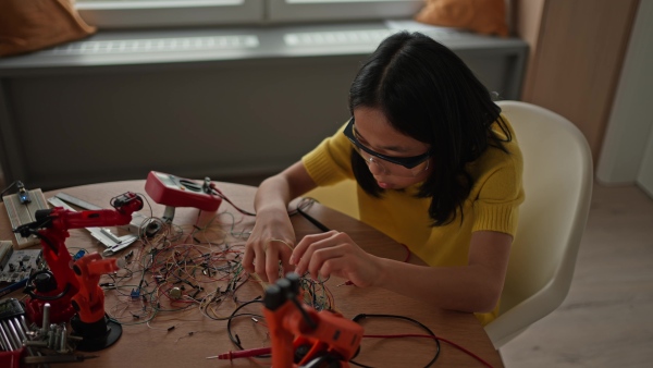 Curious young Japanese girl assembling her first DIY robot at home, exploring robotics and STEM education through hands-on learning. Concept of creativity, innovation, and girls in technology.