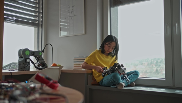 Curious young Japanese girl playing with her DIY robot at home, exploring robotics.