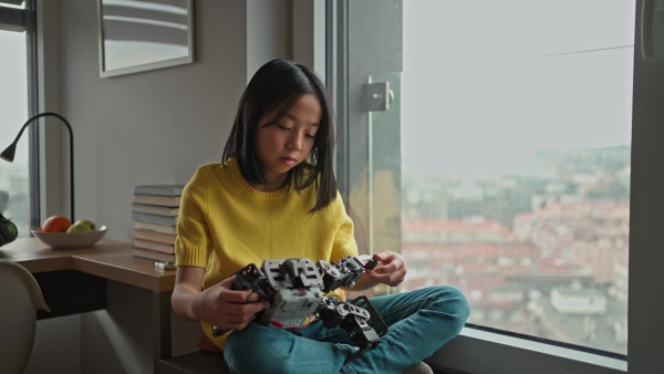 Curious young Japanese girl playing with her DIY robot at home, exploring robotics.