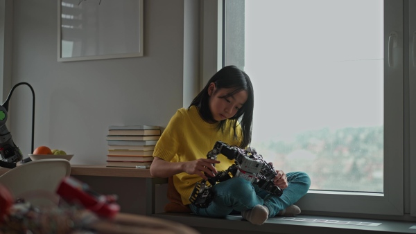 Curious young Japanese girl playing with her DIY robot at home, exploring robotics.