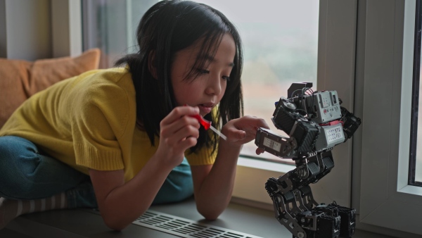 Curious young Japanese girl playing with her DIY robot at home, exploring robotics.
