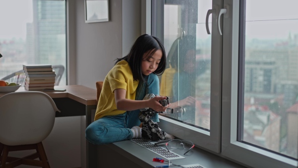 Curious young Japanese girl playing with her DIY robot at home, exploring robotics.