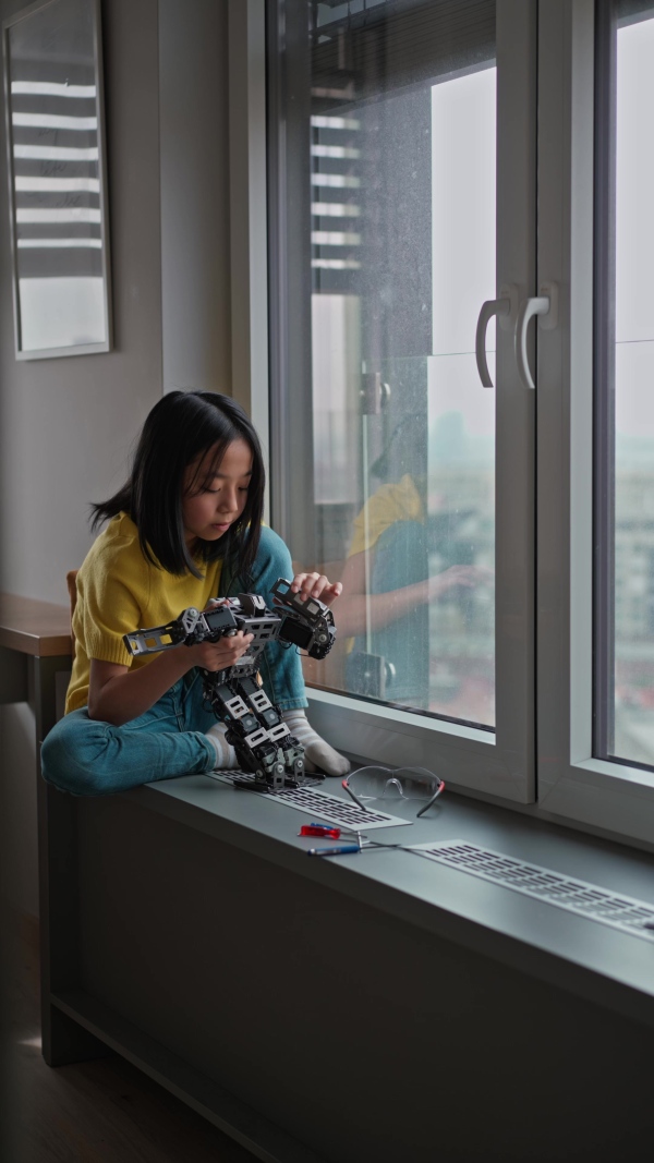 Curious young Japanese girl playing with her DIY robot at home, exploring robotics.