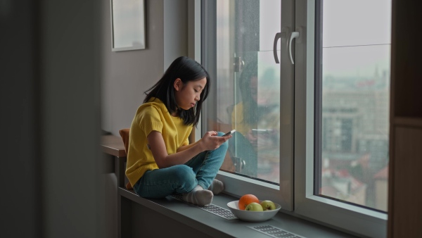 Young diabetic japanese girl with CGM sensor scrolling her smartphone next to a window.