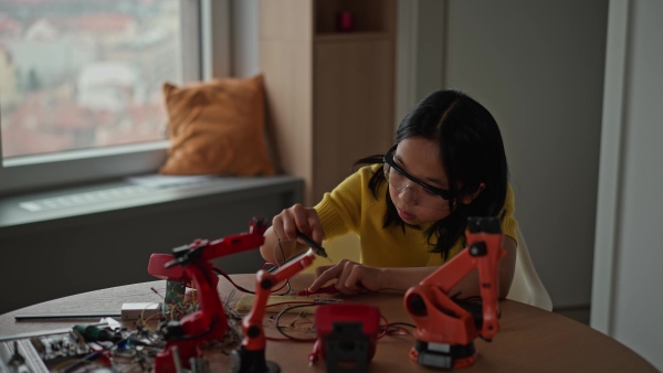 Curious young Japanese girl assembling her first DIY robot at home, exploring robotics and STEM education through hands-on learning. Concept of creativity, innovation, and girls in technology.