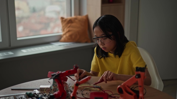 Curious young Japanese girl assembling her first DIY robot at home, exploring robotics and STEM education through hands-on learning. Concept of creativity, innovation, and girls in technology.