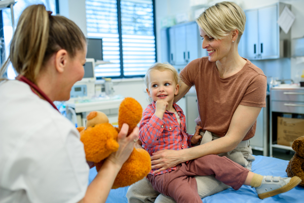 Female pediatrician comforting little boy with teddy bear during checkup