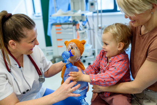 Female pediatrician demonstrates oxygen mask on teddy bear to young patient