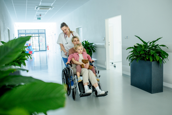 Female doctor or nurse pushing wheelchair with mother and son after treatment