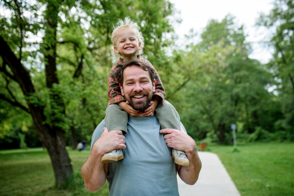 Dad carrying his smiling son on shoulders during walk in park
