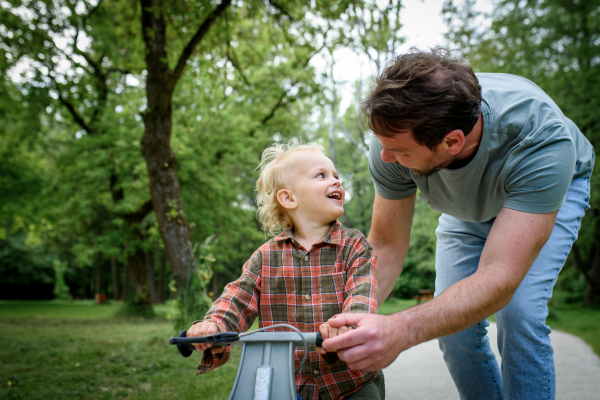 Proud dad watching son ride his balance bike in park.