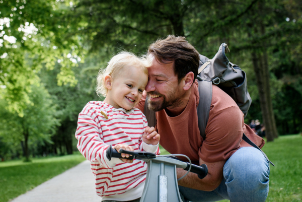Father encourages son riding balance bike in park, hugging him.