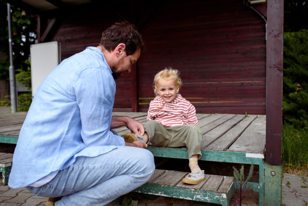Father helping little son with shoes, sitting on wooden steps.