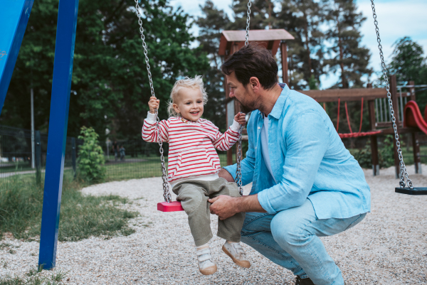 Father swinging small son on playground swing, weekend fun.