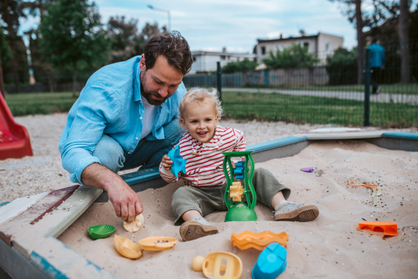 Father and little toddler son playing in the sandbox on playground, weekend fun.