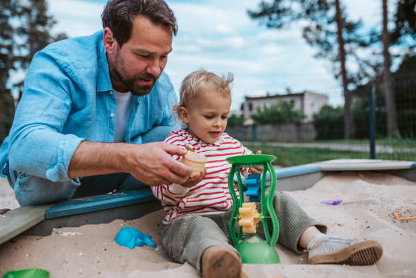 Father and little toddler son playing in the sandbox on playground, weekend fun.