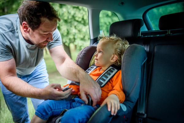 Toddler frowns while dad buckles him into car seat, leaving playground.