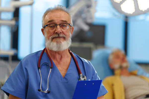 Portrait of older doctor standing in examination room in hospital.