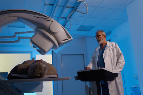 Radiologist performing X-ray examination on male patient using a tilting radiographic wall stand.