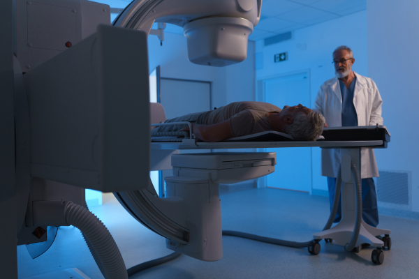 Male patient undergoing X-ray examination using a tilting radiographic wall stand.