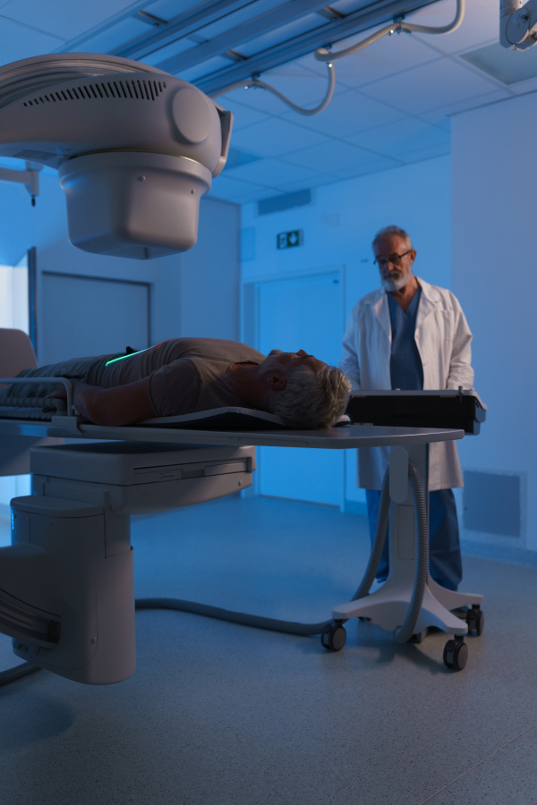 Male patient undergoing X-ray examination using a tilting radiographic wall stand.