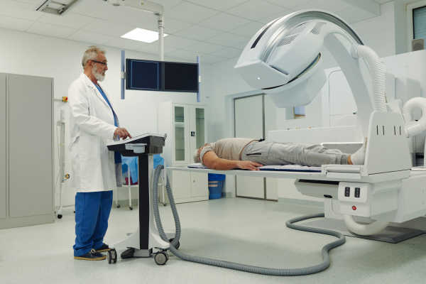 Male patient undergoing X-ray examination using a tilting radiographic wall stand.