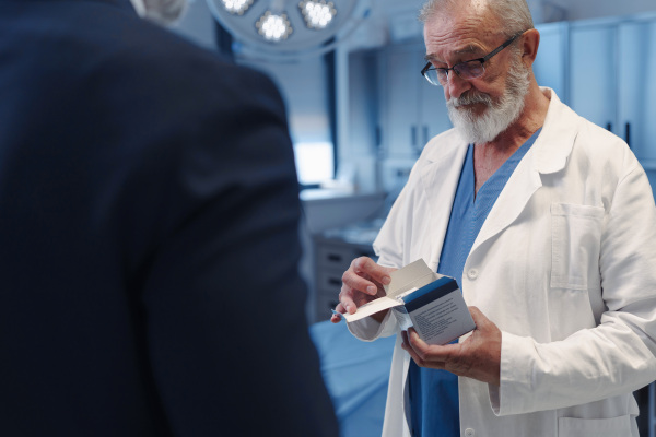 Confident medical sales representative introducing pharmaceutical products to doctor. Hospital setting.