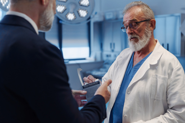 Confident medical sales representative introducing pharmaceutical products to doctor. Hospital setting.