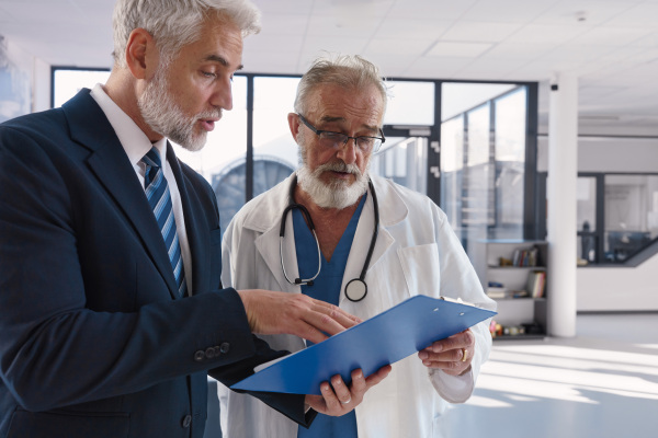 Doctor talking with hospital manager, showing him document.