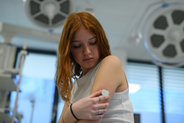 Teenage girl with diabetes checking CGM sensor on arm during hospital visit.