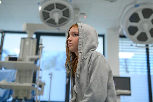 Teenage girl in hoodie waiting for medical examination in hospital.