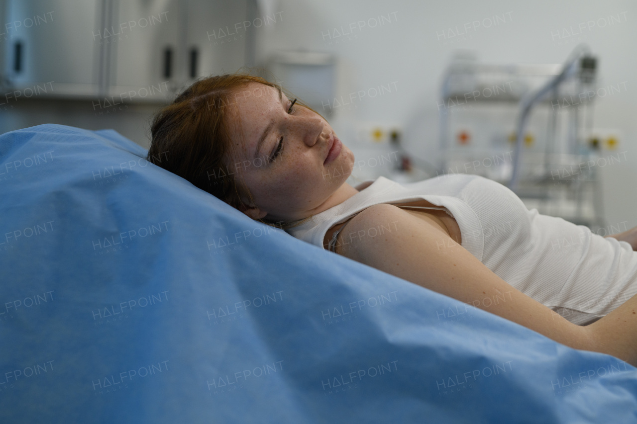 Teenage girl waiting for medical examination, lying on hospital bed in tank top.